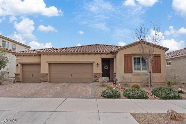 mediterranean / spanish-style house with stucco siding, decorative driveway, stone siding, a garage, and a tiled roof