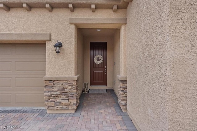 entrance to property featuring a garage, stone siding, and stucco siding