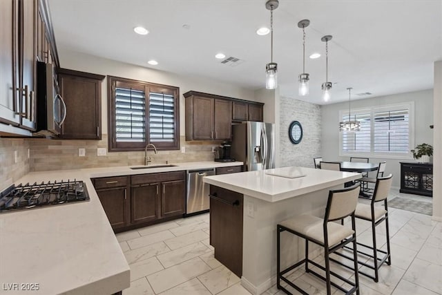 kitchen with dark brown cabinetry, a breakfast bar, marble finish floor, stainless steel appliances, and a sink