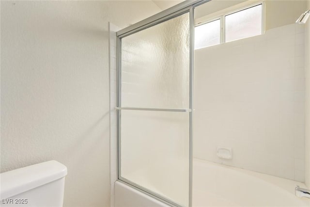 bathroom featuring toilet and shower / bath combination with glass door