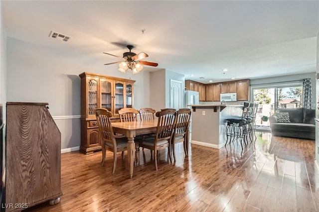 dining space with light wood-style flooring, a ceiling fan, visible vents, and baseboards