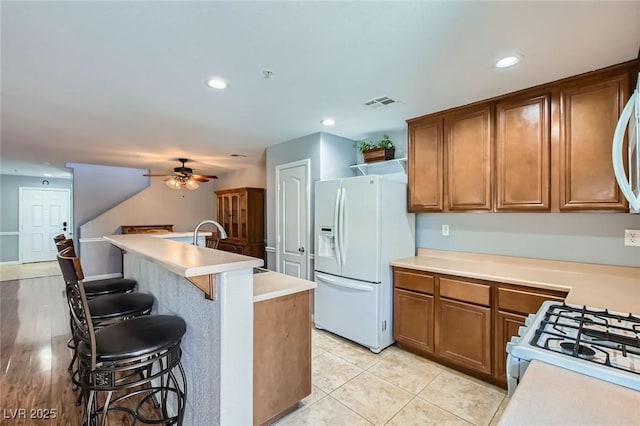 kitchen featuring white appliances, a ceiling fan, brown cabinetry, visible vents, and light countertops