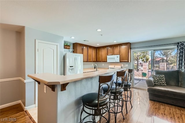 kitchen with white appliances, baseboards, light countertops, a kitchen breakfast bar, and light wood-type flooring