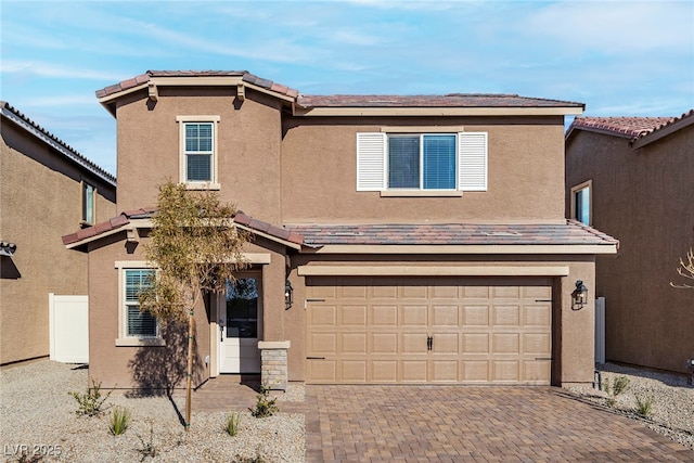 traditional-style house featuring stucco siding, a tile roof, decorative driveway, and a garage