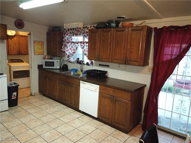 kitchen featuring dark countertops, vaulted ceiling, white appliances, washer / clothes dryer, and a sink