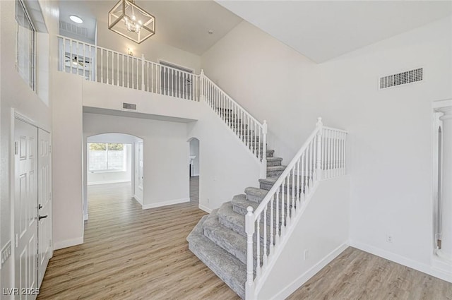 stairway with arched walkways, visible vents, a towering ceiling, and wood finished floors