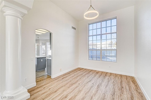 empty room featuring visible vents, baseboards, wood finished floors, arched walkways, and ornate columns