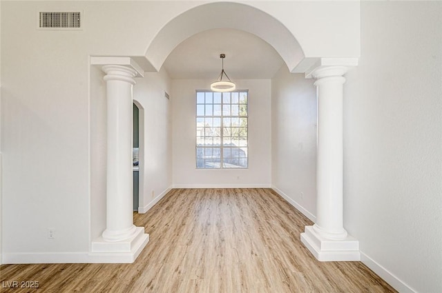 unfurnished dining area featuring arched walkways, visible vents, baseboards, and wood finished floors