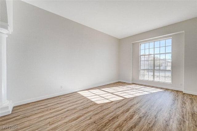 unfurnished room with baseboards, wood finished floors, and ornate columns