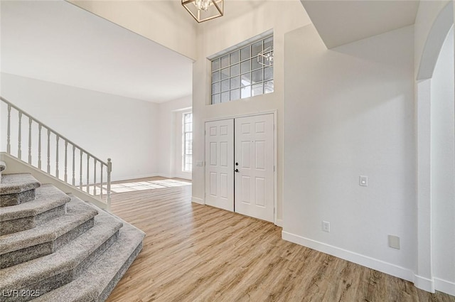 foyer with stairway, wood finished floors, baseboards, and a chandelier