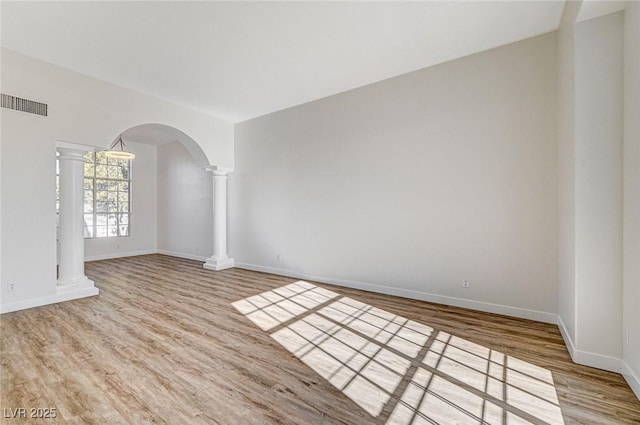 spare room with wood finished floors, visible vents, baseboards, decorative columns, and arched walkways