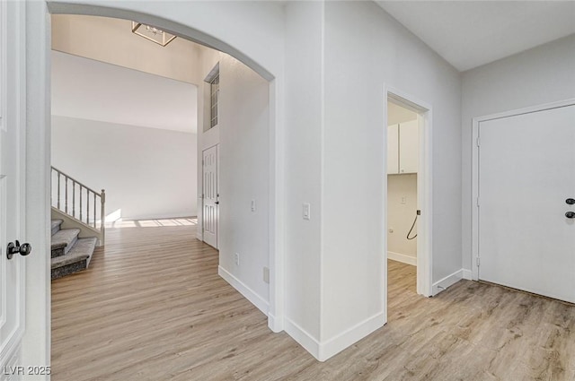 corridor with light wood finished floors, arched walkways, stairs, and baseboards