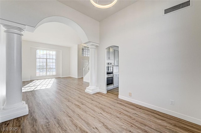 unfurnished room featuring wood finished floors, visible vents, baseboards, decorative columns, and arched walkways