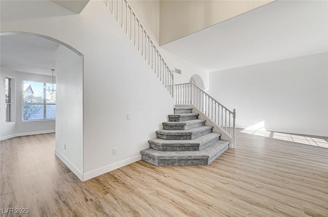 stairway with arched walkways, visible vents, baseboards, and wood finished floors