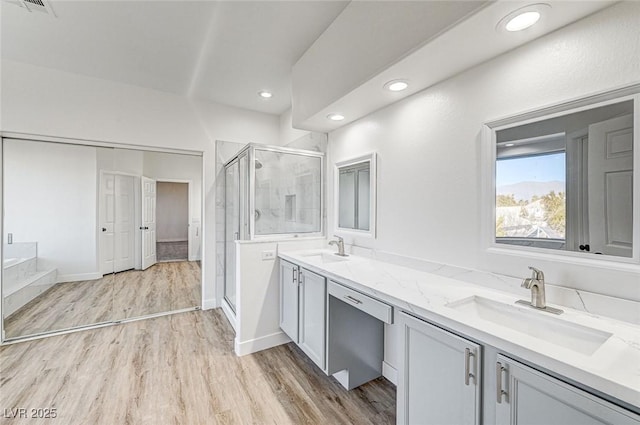 full bath with double vanity, wood finished floors, a stall shower, and a sink