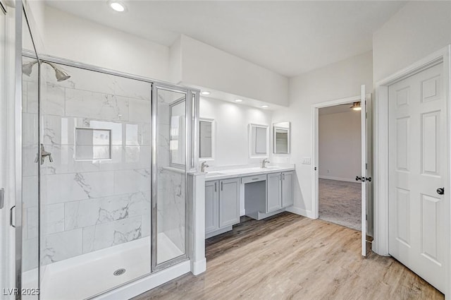 full bathroom with double vanity, a stall shower, wood finished floors, and a sink