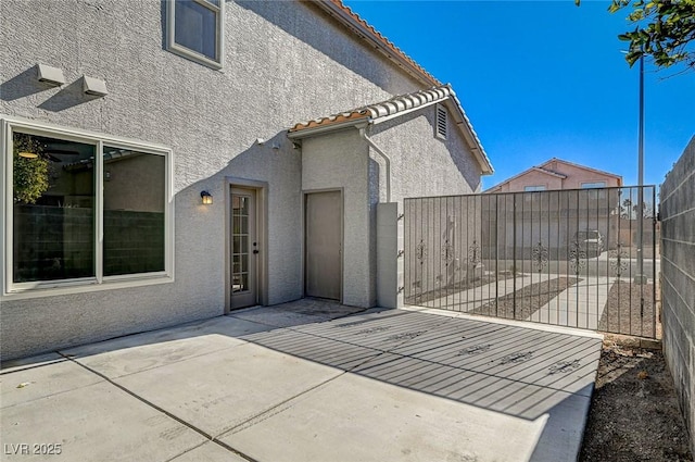 view of home's exterior featuring fence, a tile roof, stucco siding, a patio, and a gate