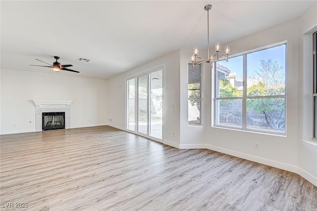 unfurnished living room with visible vents, ceiling fan with notable chandelier, a fireplace, and wood finished floors