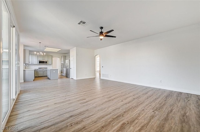 unfurnished living room with light wood finished floors, visible vents, and ceiling fan with notable chandelier