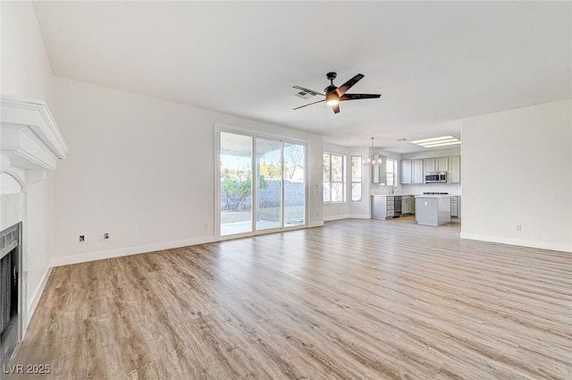 unfurnished living room featuring visible vents, a fireplace, light wood-type flooring, and a ceiling fan