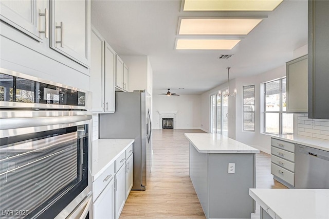 kitchen with light wood-style flooring, ceiling fan with notable chandelier, open floor plan, stainless steel appliances, and a fireplace