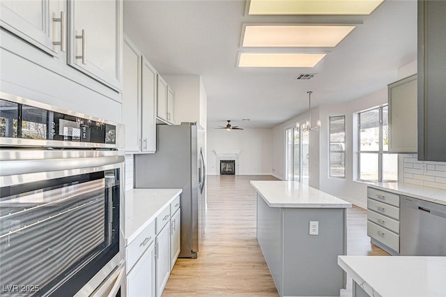 7900 Holly Knoll Ave, Las Vegas, NV 89129 - kitchen featuring light wood finished floors, a fireplace, appliances with stainless steel finishes, open floor plan, and ceiling fan with notable chandelier