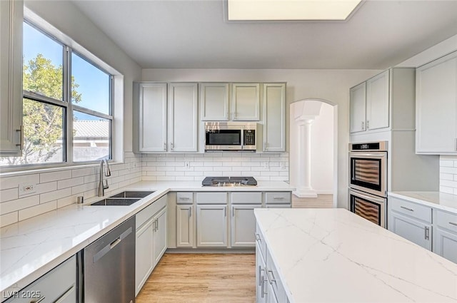 kitchen with arched walkways, appliances with stainless steel finishes, tasteful backsplash, and a sink