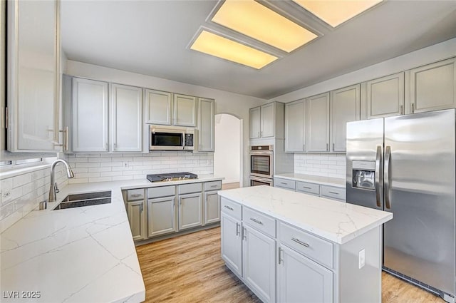 kitchen featuring light wood-type flooring, light stone counters, gray cabinets, appliances with stainless steel finishes, and a sink