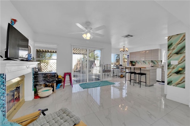 interior space with visible vents, marble finish floor, ceiling fan with notable chandelier, and a glass covered fireplace