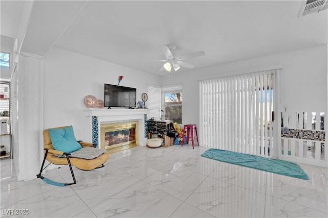 living area with a tiled fireplace, visible vents, marble finish floor, and ceiling fan