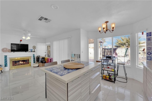 kitchen featuring visible vents, light countertops, ceiling fan with notable chandelier, a glass covered fireplace, and marble finish floor