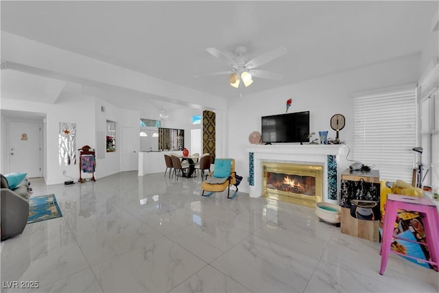 living area featuring marble finish floor, ceiling fan, and a tiled fireplace