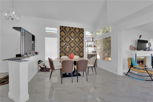 dining space with a glass covered fireplace, a notable chandelier, marble finish floor, and high vaulted ceiling