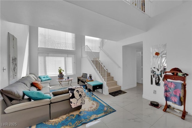 living area with stairs, baseboards, marble finish floor, and a towering ceiling