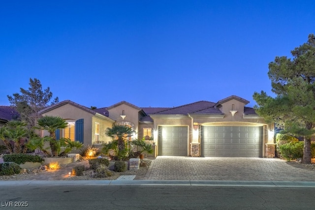 view of front facade featuring stucco siding, a tile roof, decorative driveway, and a garage