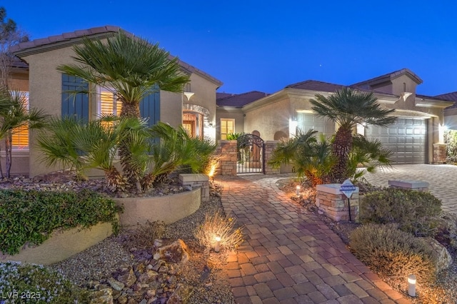 view of front of house with stucco siding, decorative driveway, a garage, and a gate