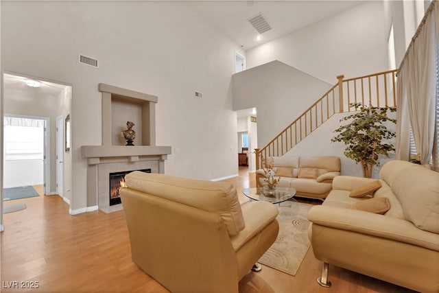 living area featuring baseboards, visible vents, light wood-style flooring, stairs, and a tiled fireplace