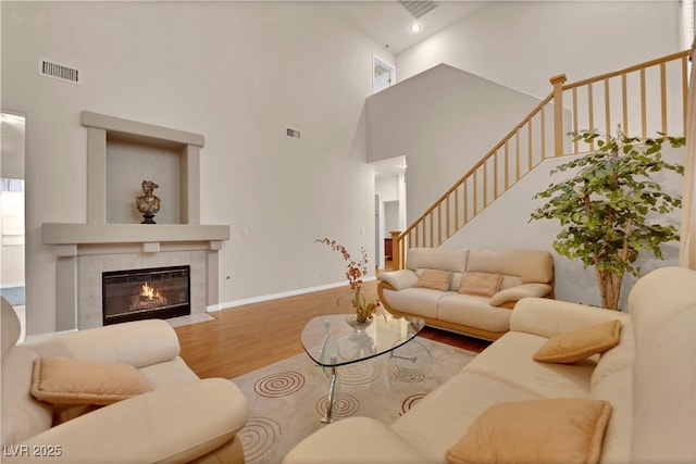 living area with a tiled fireplace, wood finished floors, visible vents, and baseboards