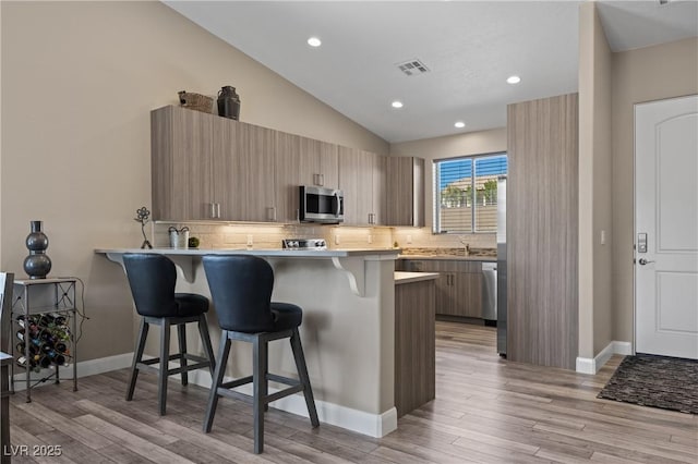 kitchen with visible vents, lofted ceiling, a kitchen breakfast bar, a peninsula, and stainless steel appliances