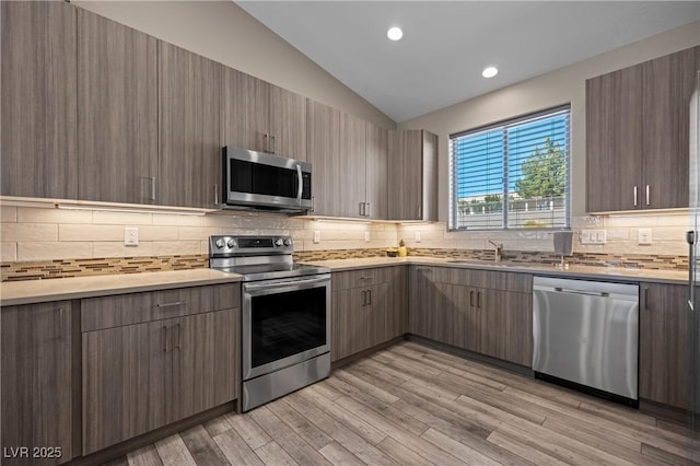 kitchen with light wood finished floors, light countertops, lofted ceiling, stainless steel appliances, and a sink