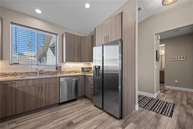 kitchen featuring a sink, decorative backsplash, light wood-style floors, and stainless steel appliances