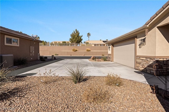 view of yard with a patio, central AC unit, fence, driveway, and an attached garage