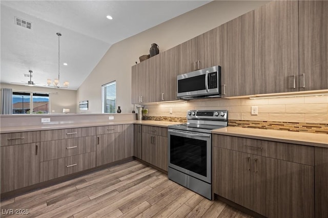 kitchen with light wood-type flooring, stainless steel appliances, light countertops, and lofted ceiling