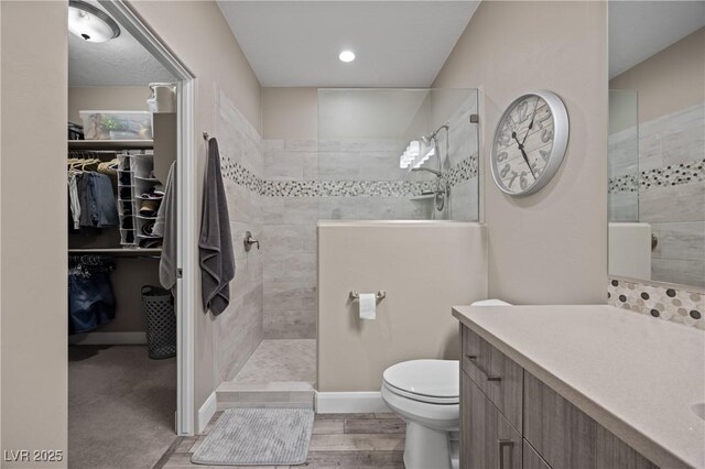 bathroom with toilet, wood finished floors, vanity, walk in shower, and a spacious closet