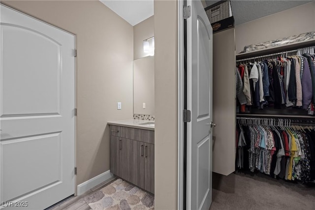 bathroom with a walk in closet, baseboards, and vanity