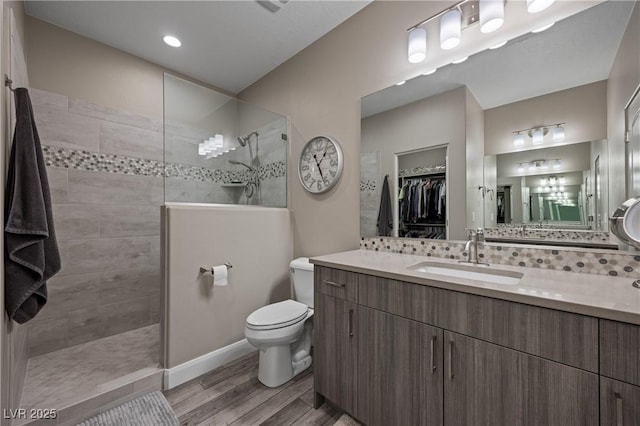 bathroom with toilet, wood finished floors, vanity, walk in shower, and a spacious closet