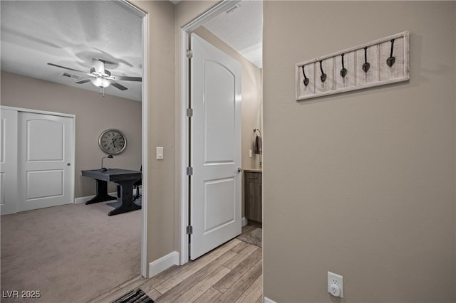 hall with light wood-type flooring, visible vents, baseboards, and light carpet