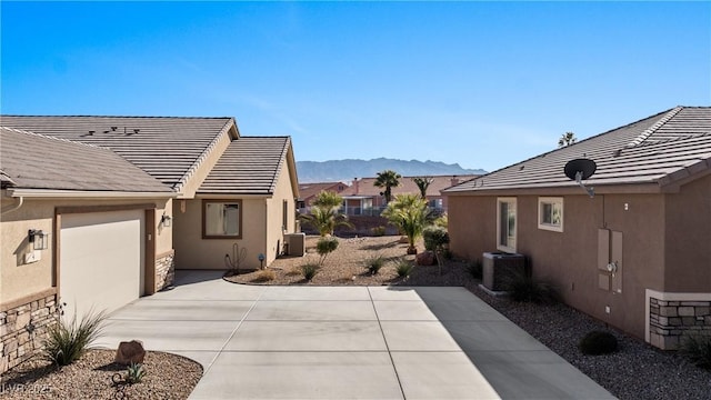 view of property exterior with central AC unit, stucco siding, concrete driveway, a garage, and a mountain view