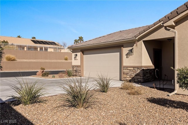 view of property exterior featuring stucco siding, driveway, stone siding, a garage, and a tiled roof