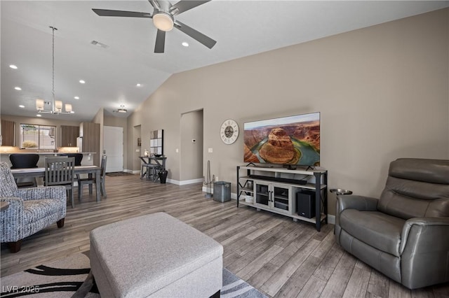 living area featuring visible vents, ceiling fan with notable chandelier, light wood finished floors, baseboards, and vaulted ceiling